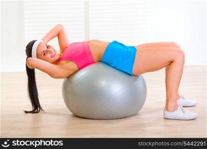 Smiling fitness girl doing abdominal crunch on fitness ball at home&#xA;