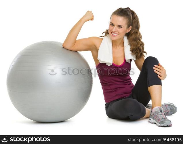 Smiling fitness young woman sitting near fitness ball and showing biceps