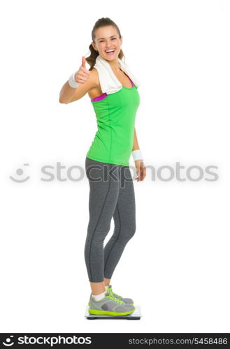 Smiling fitness young woman standing on scales and showing thumbs up