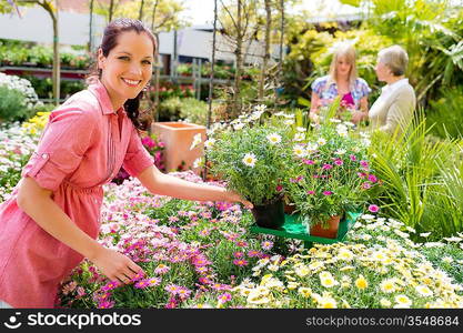 Smiling florist arranging flower pots in garden center greenhouse store