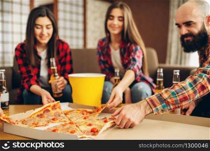 Smiling friends drinks beer with pizza at the house party. Good friendship, group of people leisures together. Cheerful company celebrate the event