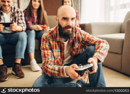 Smiling friends with joysticks plays tv console at home. Group of gamers with joypads playing videogame, male and female players with gamepads. Friends with joysticks plays tv console at home