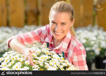 Smiling garden center woman worker with potted daisy flowers sunny