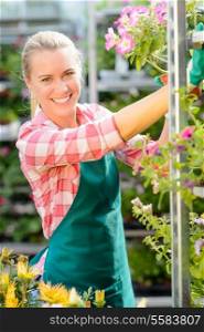Smiling garden center woman working with potted flowers sunny day