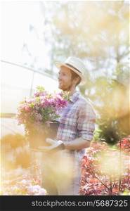 Smiling gardener looking away while holding flower pot outside greenhouse