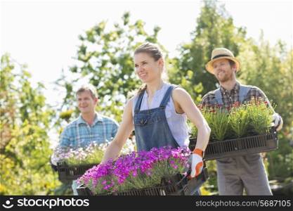 Smiling gardeners carrying crates with flower pots at plant nursery
