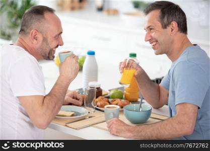 smiling gay couple talking and eating breakfast together