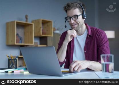 Smiling German guy in casual clothes sitting at home in wireless headset and taking part in online meeting with colleagues, male freelancer using laptop computer during video call with client. Smiling German guy sitting at home in wireless headset and taking part in online meeting