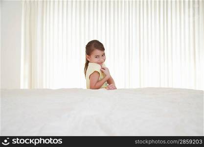Smiling girl (5-6) behind bed