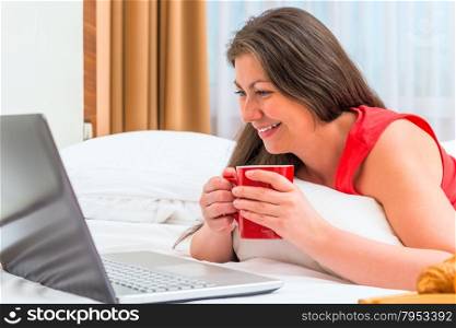 smiling girl attentively looks at a laptop and drinking tea