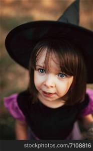 Smiling girl disguised as a witch in the woods during Halloween