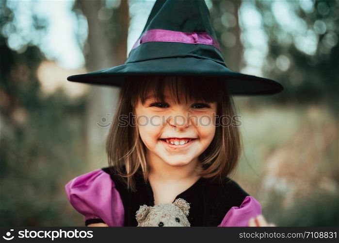 Smiling girl disguised as a witch in the woods during Halloween