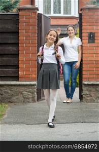 Smiling girl going out the house to school. Mother standing in doorway and waving to her
