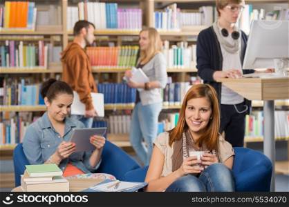 Smiling girl having coffee with students in background at library