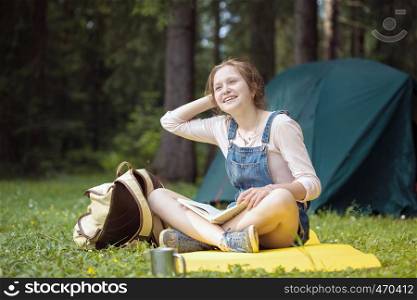 smiling girl hiker sitting and reading a book near the tent