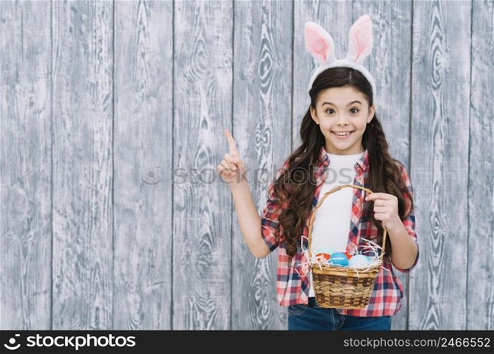 smiling girl holding easter eggs basket pointing finger looking camera
