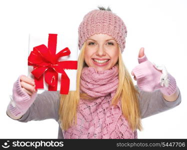 Smiling girl in winter clothes showing christmas presenting box and showing thumbs up