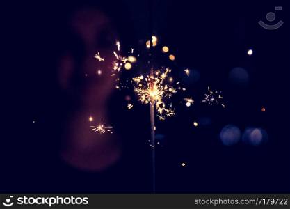 Smiling girl is holding a sparkler in her hand, indoor, lights in background