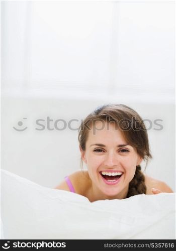 Smiling girl laying in bed and hiding behind pillow