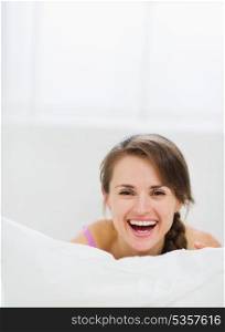 Smiling girl laying in bed and hiding behind pillow
