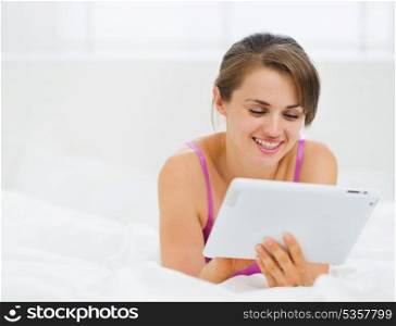 Smiling girl laying in bed and using tablet PC
