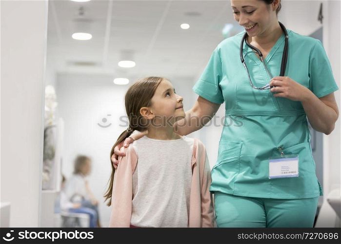 Smiling girl looking at mid adult nurse while walking in hospital corridor