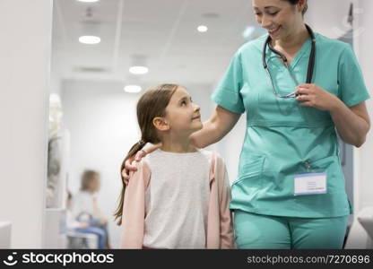 Smiling girl looking at mid adult nurse while walking in hospital corridor