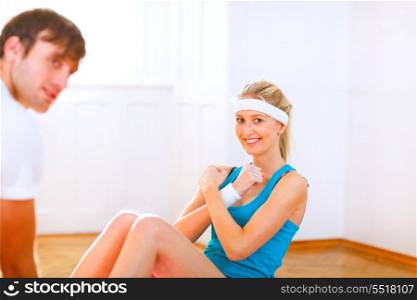 Smiling girl making abdominal crunch assisted by her personal trainer &#xA;