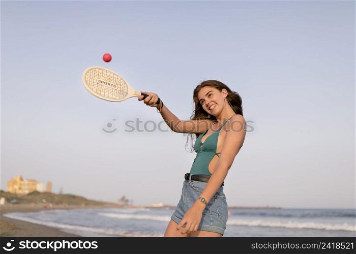 smiling girl playing with tennis ball racket beach