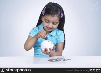 Smiling girl putting coins in piggy bank against blue background