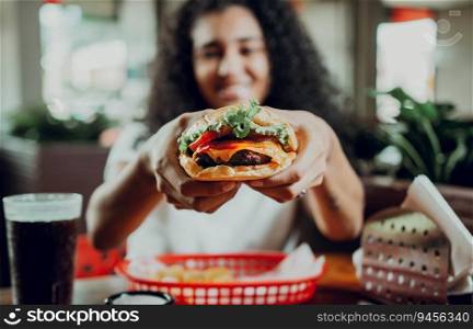 Smiling girl showing a burger in a restaurant. Close-up of a woman showing appetizing hamburger in a restaurant