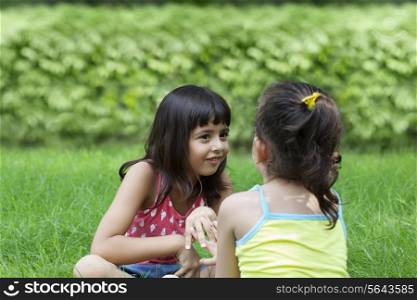 Smiling girl sitting in park talking to her sister