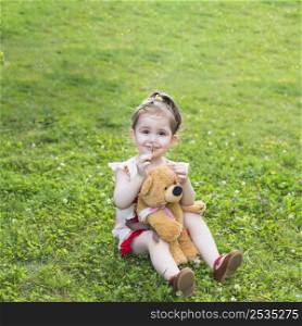 smiling girl sitting with teddy bear smelling flower park