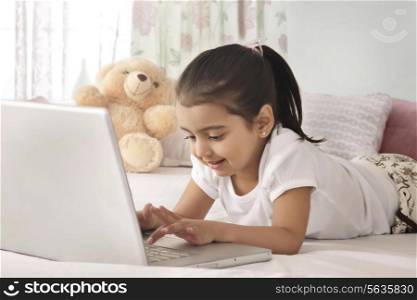 Smiling girl using laptop in bed