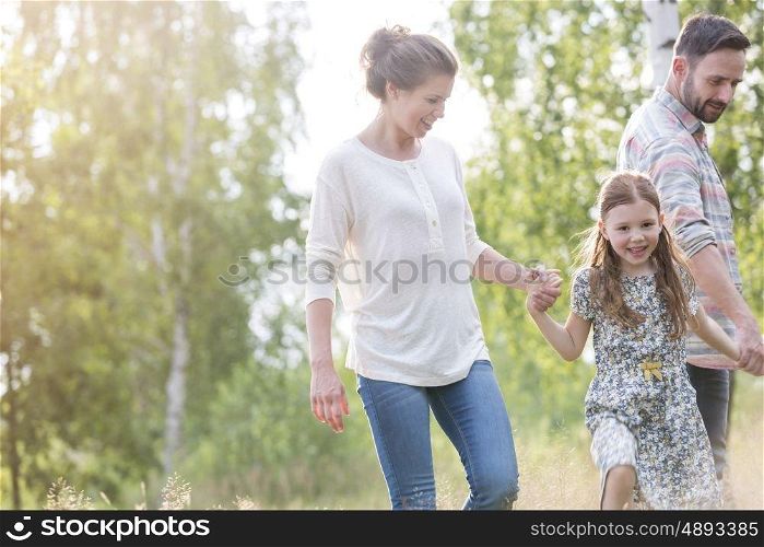 Smiling girl walking with parents against trees on field