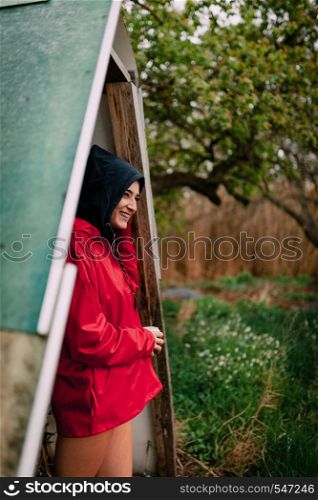 Smiling girl wearing red raincoat takes shelter from the rain