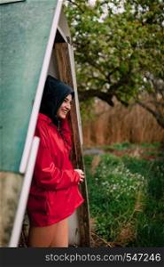 Smiling girl wearing red raincoat takes shelter from the rain