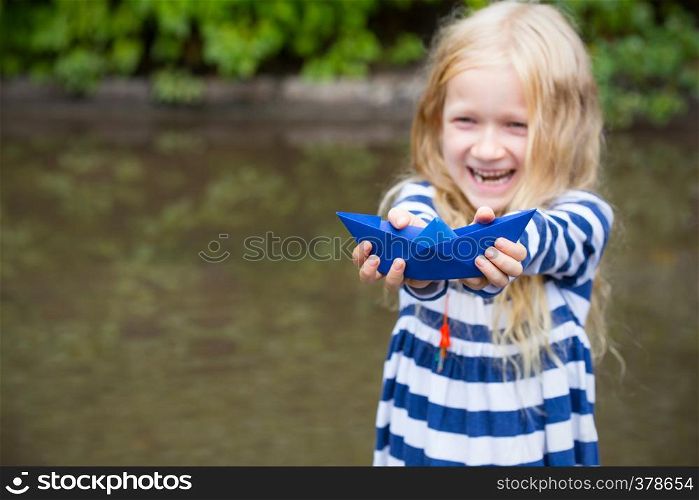 smiling girl with blue paper boat in a puddle after the rain, summer