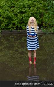 smiling girl with blue paper boat in a puddle after the rain, summer