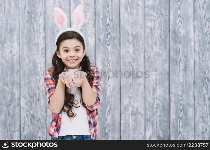 smiling girl with bunny ears posing like rabbit against gray wooden desk