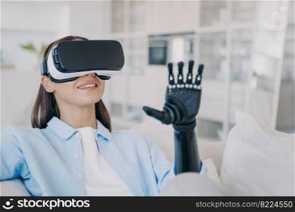 Smiling girl with disability wearing VR glasses interacting with 3d virtual reality objects in cyberspace, using artificial limb, bionic prosthetic arm. Rehabilitation disabled people.. Girl in VR glasses interacts with virtual reality by prosthetic arm. Rehabilitation disabled people
