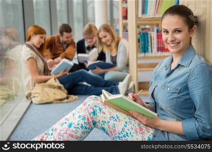 Smiling girl with group of students studying in university library