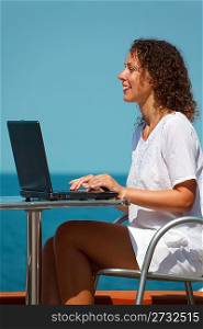 Smiling girl with laptop. Sits at table on beach, warm sunny day. Vertical format.