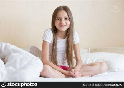 Smiling girl with long dark hair sitting on bed