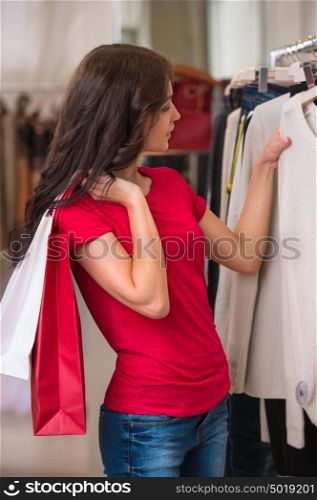 Smiling girl with shopping bags at store choosing clothes