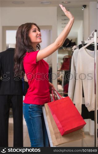 Smiling girl with shopping bags at store waving her hand to friends or sales person for asking help