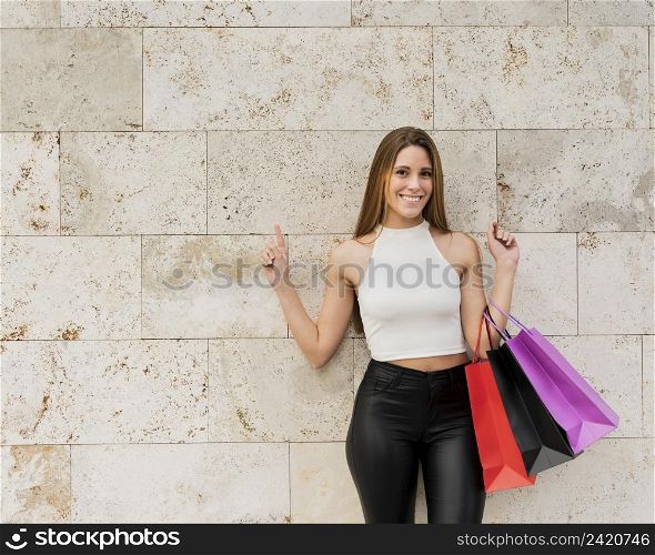 smiling girl with shopping bags standing by wall