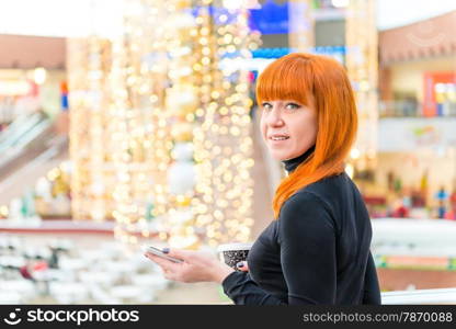 smiling girl with the phone and coffee in the mall