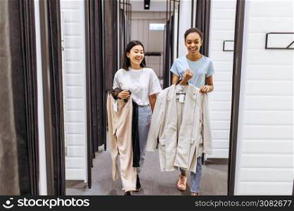 Smiling girls buying clothes in clothing store. Women shopping in fashion boutique, shopaholics, shoppers trying on garment in fitting room. Smiling girls buying clothes in clothing store