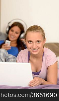 Smiling girls studying on laptop her sister listening music